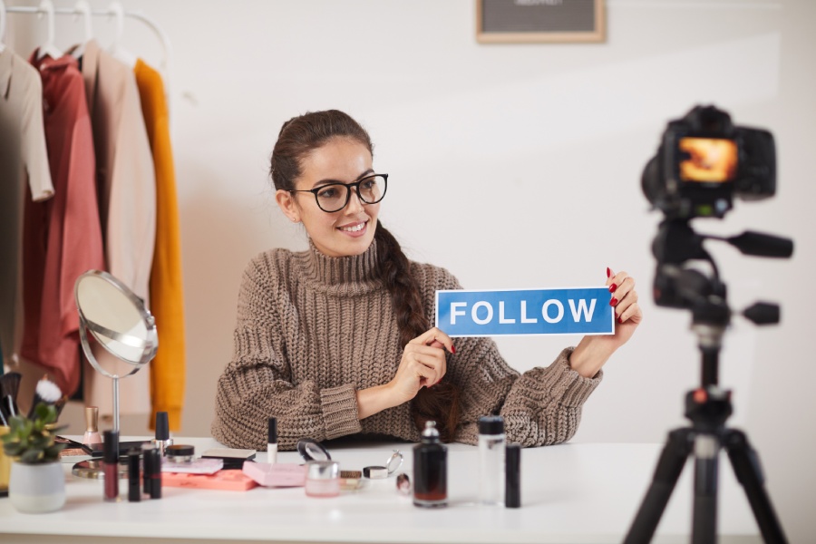 Una joven graba un vídeo de deinfluencing mientras sostiene en sus manos un cartel con la palabra “follow”. 