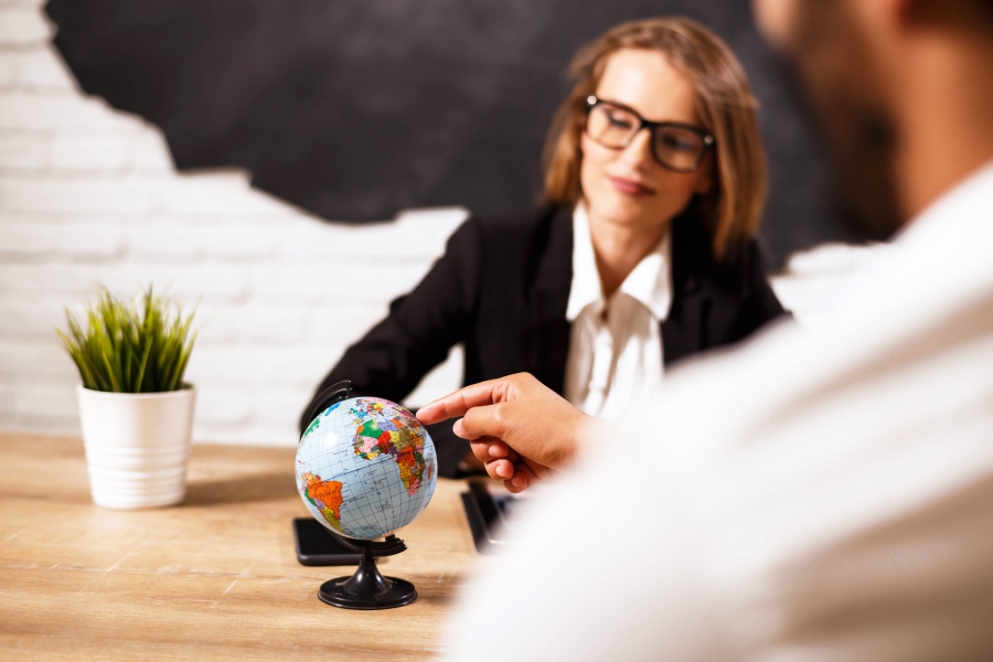 Una mujer conversa con un cliente, que señala con su dedo índice un dedo terráqueo. 